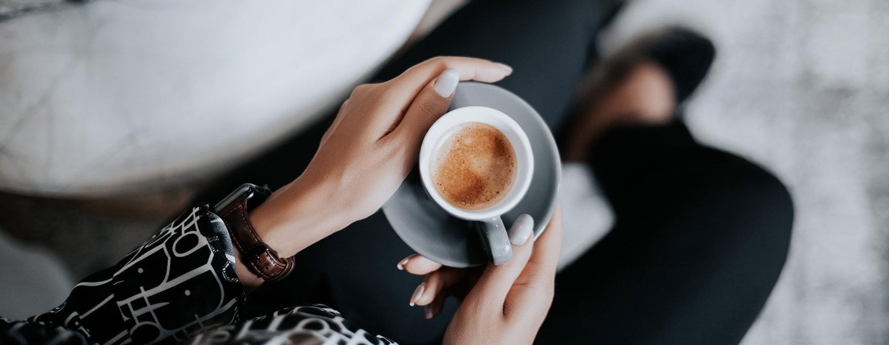 business woman sits next to a marble table with books and holds a saucer with a cup of espresso